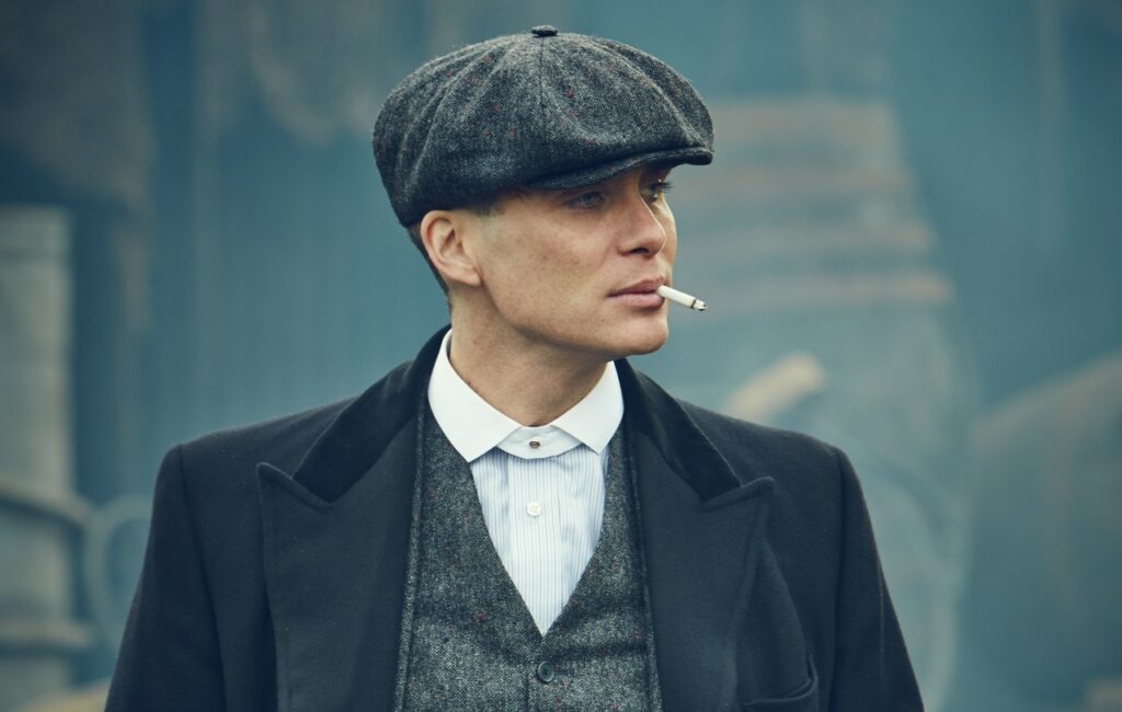 Cillian Murphy plays Tommy Shelby in 'Peaky Blinders', wearing a cap and smoking a cigarette, Unveiling the Timeless Elegance of Cillian Murphy's Style.