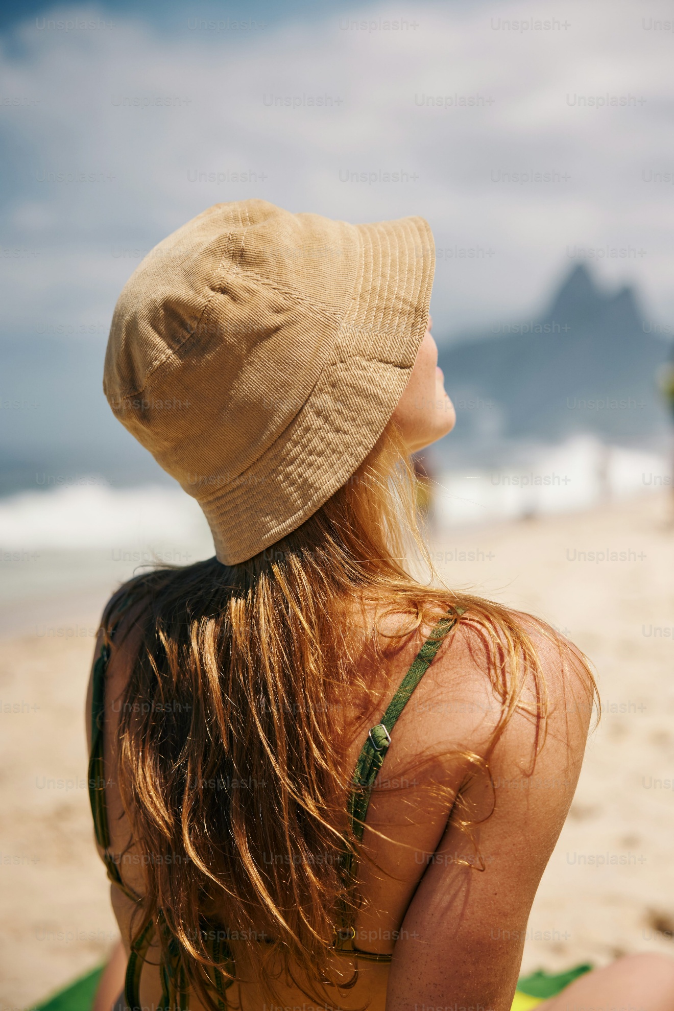 a-woman-in-a-hat-sitting-on-the-beach a woman in a hat sitting on the beach tanning her skin