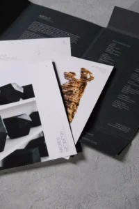 Fashion student confidently presenting open physical portfolio during review session with professor and peers modern studio setting